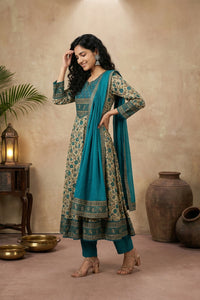 Woman in a traditional outfit with a blue dupatta standing in a decorated room.