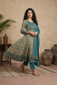 Woman in a teal and beige traditional outfit standing in a room with decorative elements.