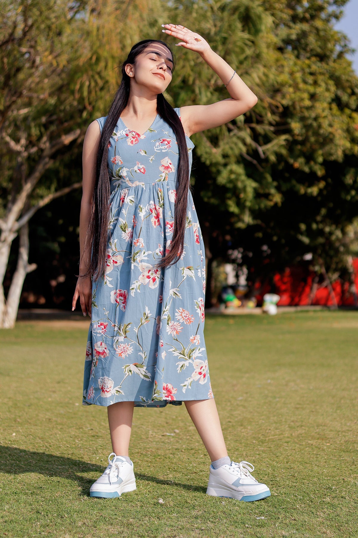 Woman in a floral dress standing on grass with trees in the background
