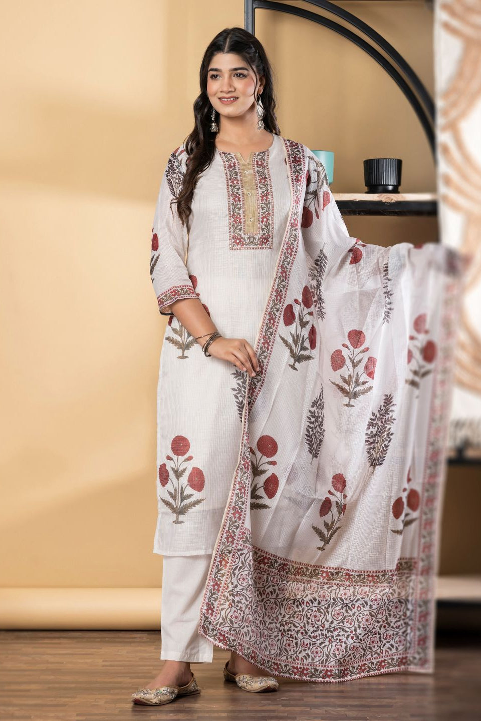 Woman wearing a white traditional outfit with red floral patterns in a room.