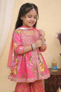 A young girl smiling and posing in a Pink Embroidered  Floral Peplum Style Kurta with Sharara and Dupatta from Desi Trove