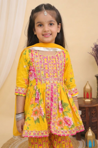 A young girl modeling a Yellow Embroidered Floral Peplum Style Kurta with Sharara and Dupatta from Desi Trove , set against a warm beige background with decorative lanterns.