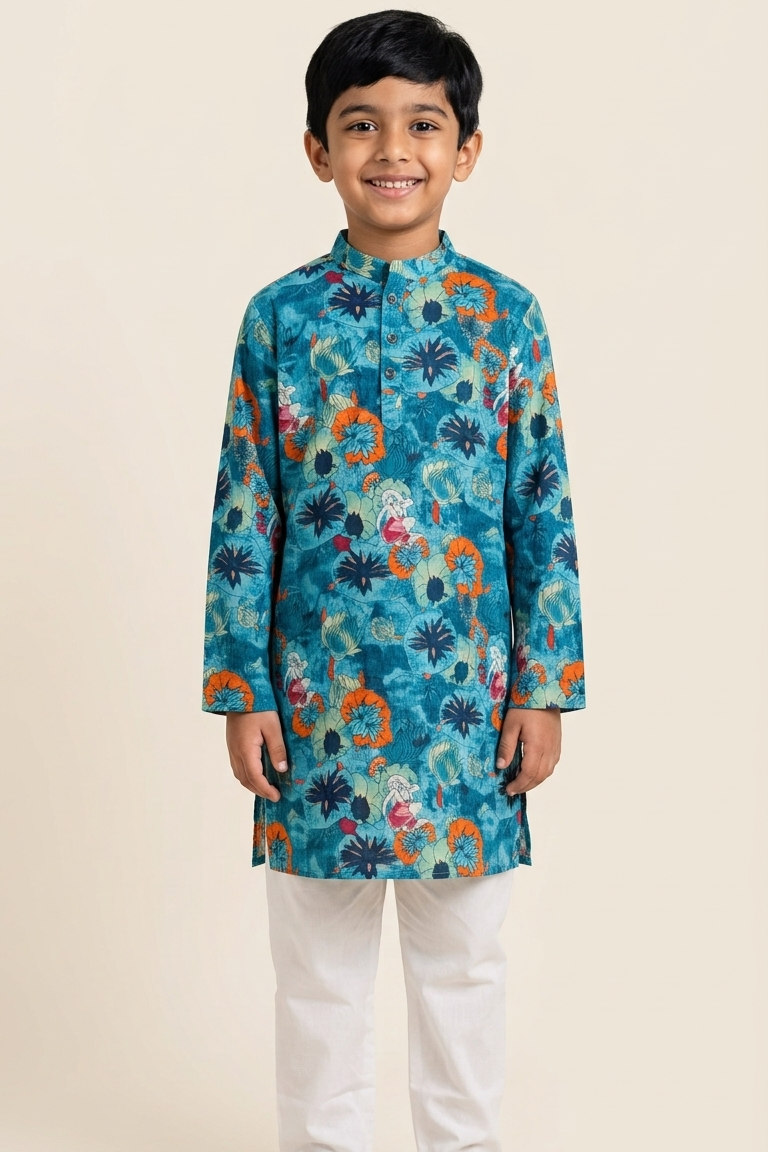 A young boy modeling a teal blue kurta with a colorful floral and paisley print, paired with white trousers and brown sandals, standing against a solid beige background.