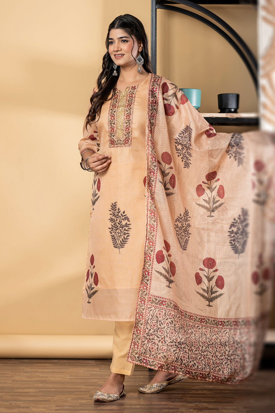 Woman wearing a beige embroidered outfit with a matching dupatta in an indoor setting.