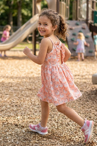Young girl in a peach chicken print dress running on a playground