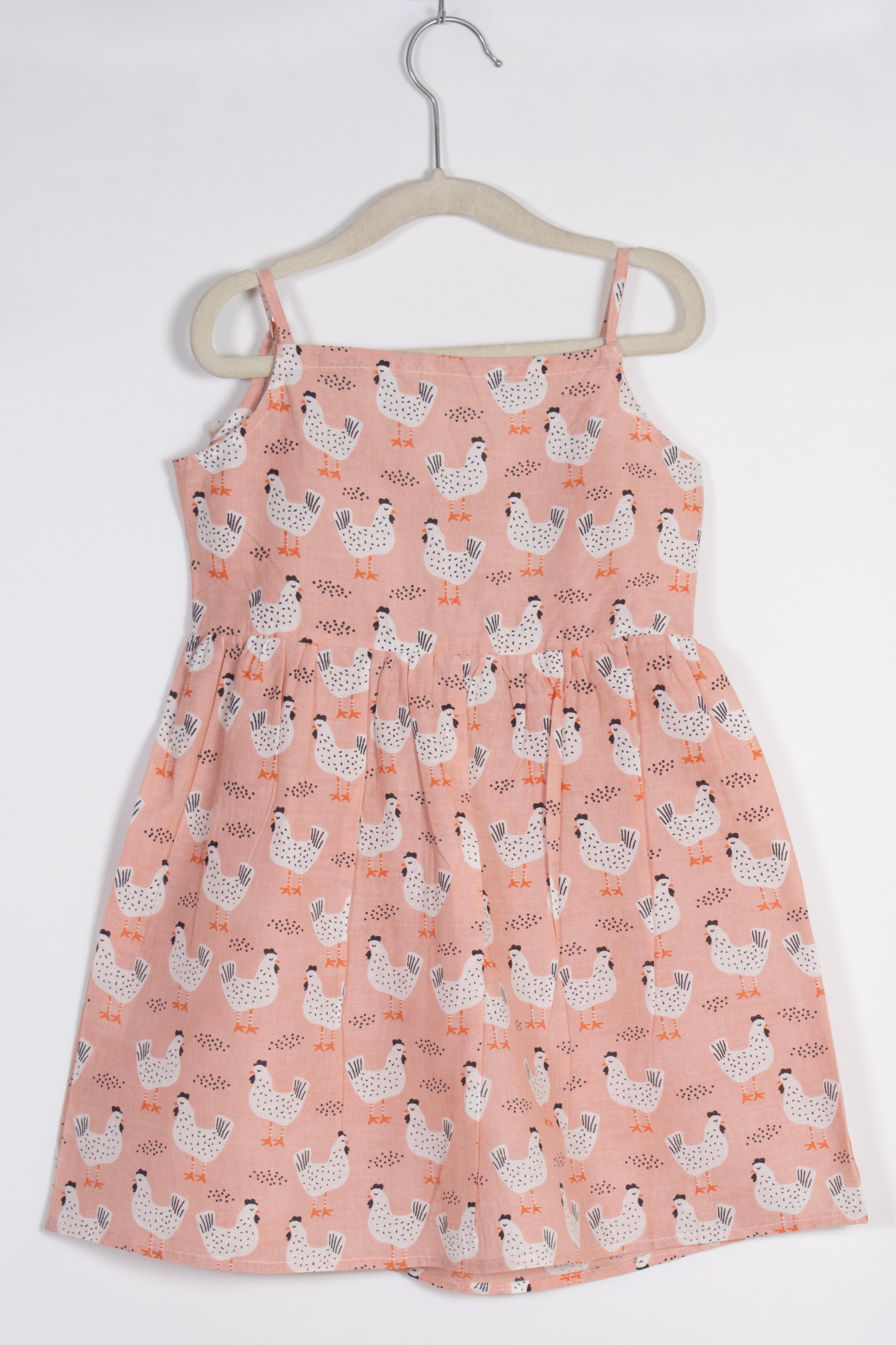 peach dress with chicken pattern on a hanger against a white background