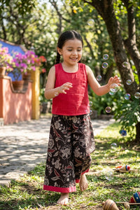 Young girl wearing red tank top and patterned culotte playing with bubbles in a garden
