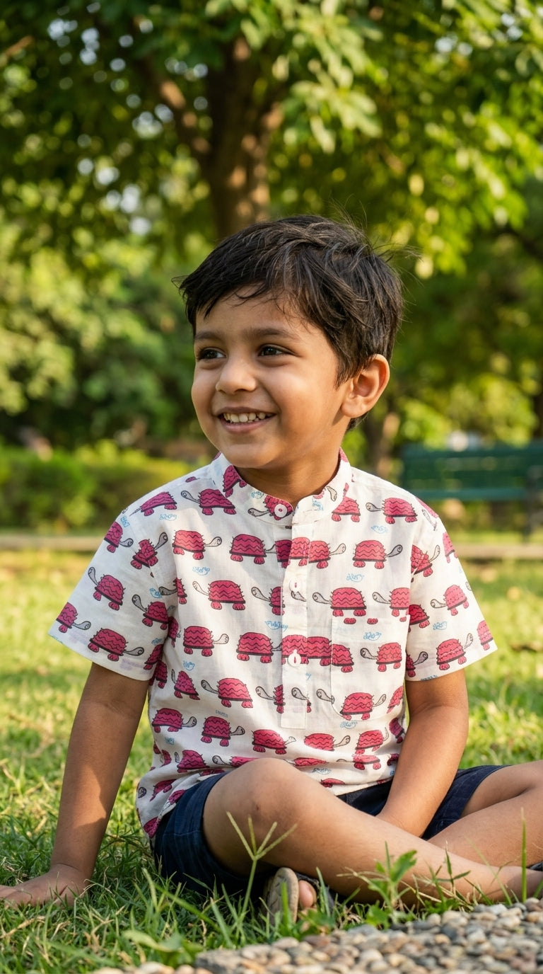 Child wearing a shirt with red turtle pattern sitting on grass
