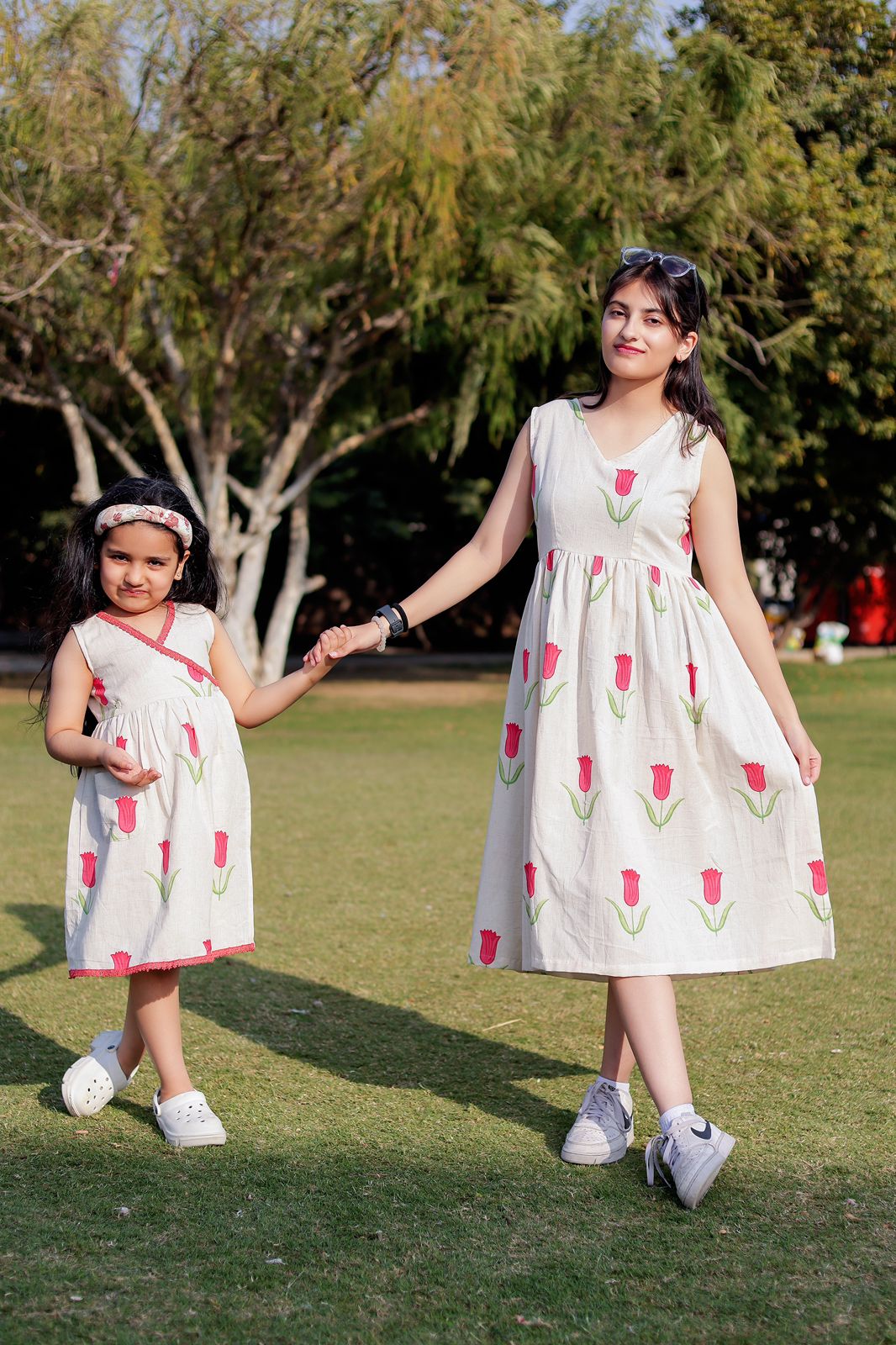 Mon and kid twinning  in matching  tulip print dresses standing on grass with trees in the background